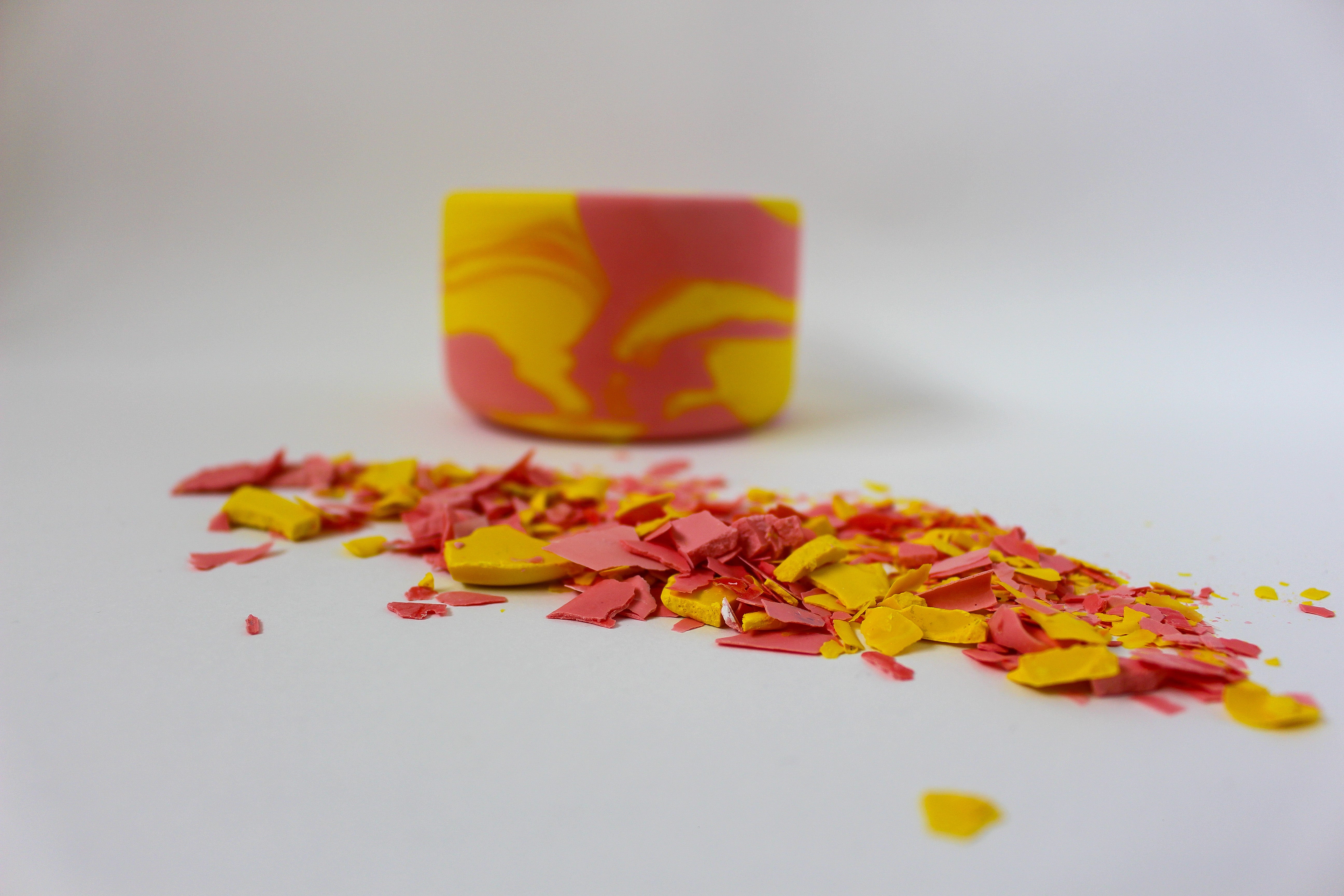 Front view of a handmade decorative bowl with a marbled pink and yellow pattern, shaped like a Yin Yang symbol with two compartments. Broken terrazzo chips in pink and yellow are in focus in the foreground.